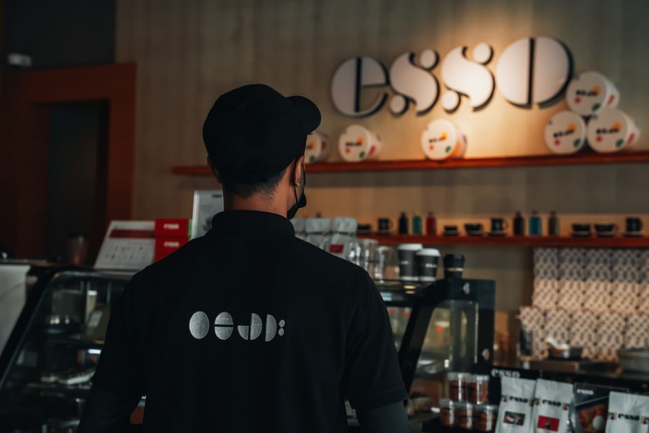 A barista in a modern coffee shop with stylish decor and signage, facing the counter.